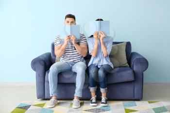 Young couple reading books while sitting on sofa at home�