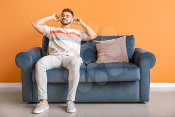 Young man listening to music while sitting on sofa at home�