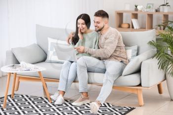 Young couple with laptop sitting on sofa at home�