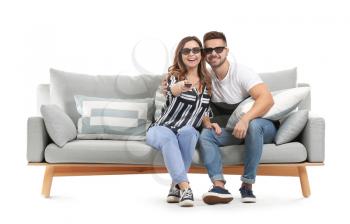 Young couple watching TV while sitting on sofa against white background�