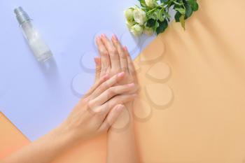 Hands of young woman and bottle of cream with flowers on color background�