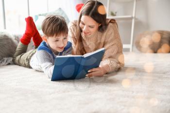Cute little boy with mother reading book at home�