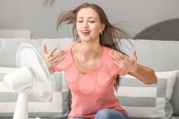 Young woman using electric fan during heatwave at home�