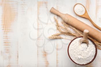 Bowl with flour and rolling pin on white wooden background�