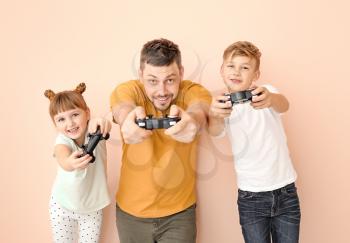 Father and his little children playing video games on color background�