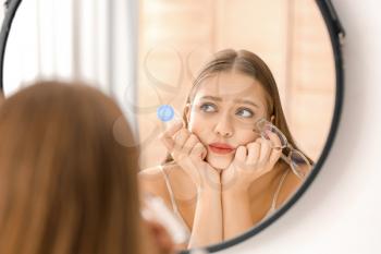 Thoughtful woman with contact lens case and eyeglasses near mirror�