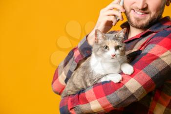 Man with cute cat talking by phone on color background�