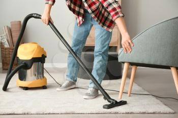 Young Asian man hoovering floor at home�