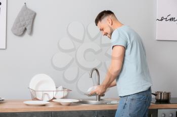 Handsome man washing dishes in kitchen�