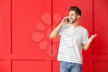 Happy young man talking by mobile phone on color background�