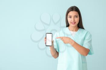 Young nurse with mobile phone on color background�