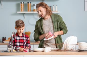 Father and son washing dishes in kitchen�