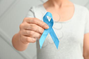 Woman with blue ribbon on grey background, closeup. Prostate cancer awareness concept�