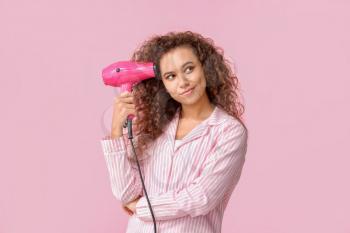 Beautiful young African-American woman with blow dryer on color background�