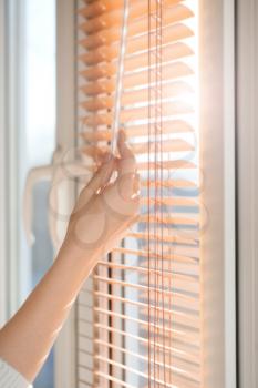 Woman opening blinds on window�