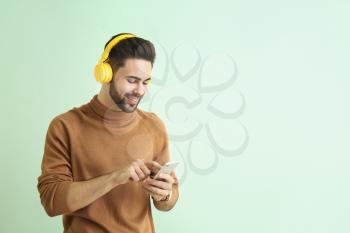 Handsome young man listening to music on color background�