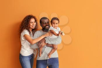 Happy African-American parents with cute baby on color background�
