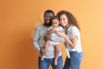 Happy African-American parents with cute baby on color background�
