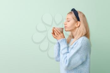 Beautiful young woman with tea on color background�