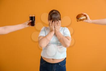 Offering of unhealthy food to sad overweight girl on color background�