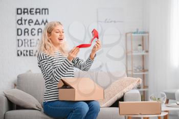 Happy young woman unpacking box with new shoes at home�