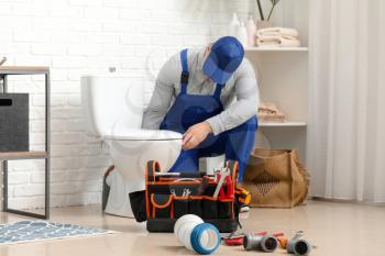 Handsome plumber repairing toilet bowl in bathroom�