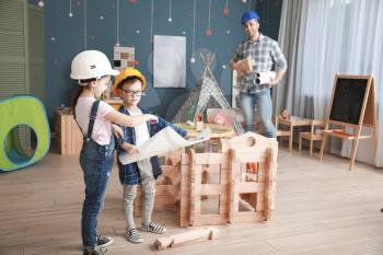 Father and little children dressed as builders playing with take-apart house at home�