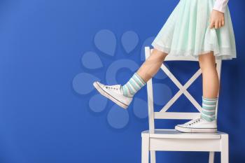 Little girl standing on chair against color background�