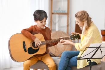 Private music teacher giving guitar lessons to little boy at home�