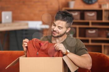 Young man unpacking box with new clothes at home�