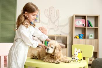 Cute little girl dressed as doctor playing with dog at home�