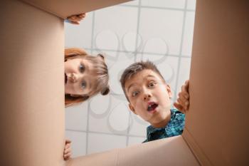 Curious children looking inside cardboard box, bottom view�