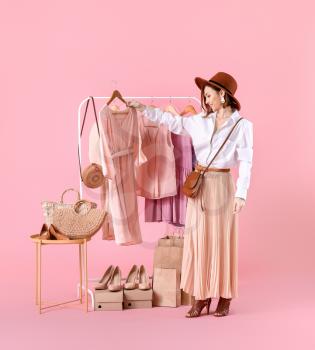 Female stylist near rack with modern clothes on color background�