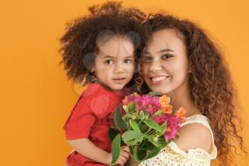 Little African-American girl with her mother and bouquet on color background�