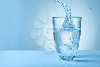 Glass of fresh water with splash on color background�