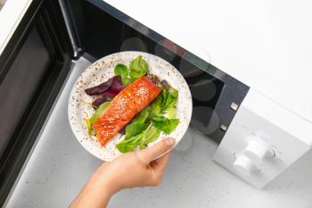 Woman putting plate with food in microwave oven�