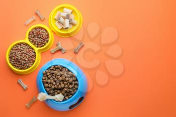 Bowls with dry pet food on color background�
