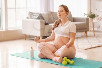 Sporty pregnant woman practicing yoga at home�