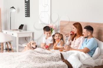Happy family having breakfast in bedroom at home�