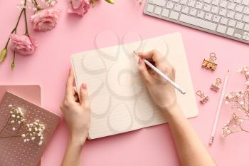 Woman writing something in notebook on color background�