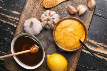 Bowl of tasty honey mustard sauce with ingredients on dark wooden background�