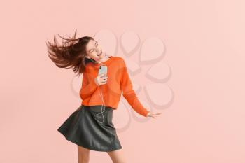 Beautiful young woman listening to music and dancing against color background�