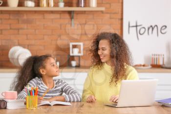 Little African-American girl with her mother doing homework in kitchen�