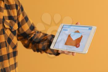 Young man with tablet computer checking his e-mail on color background�