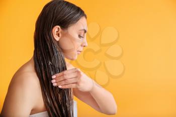 Beautiful young woman applying coconut oil on her hair against color background�