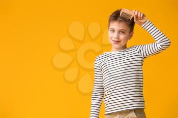 Little boy combing hair on color background�