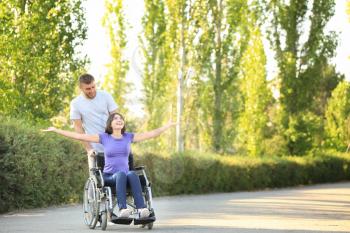 Happy young woman in wheelchair and her husband outdoors�
