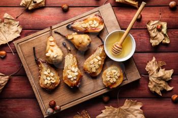 Tasty baked pears with honey and fallen leaves on wooden table�