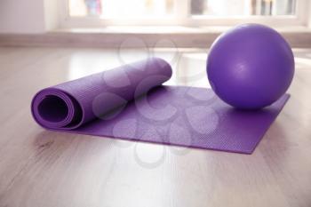 Yoga mat and ball on floor indoors�