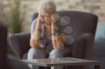 Mobile phone on table near depressed elderly woman at home�